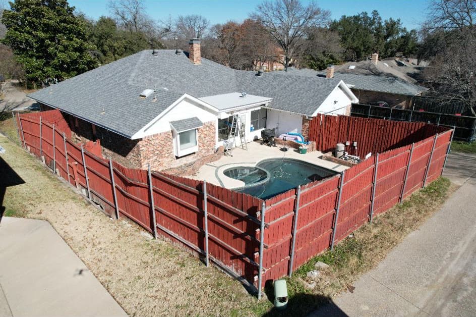 Aerial view of a backyard pool with a worn red-stained wood privacy fence